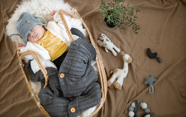 Le bébé dort doucement dans un berceau en osier dans un bonnet tricoté chaud avec une couverture chaude.