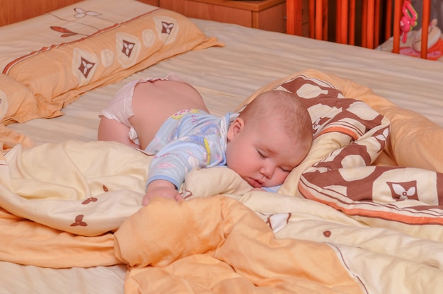 Photo le bébé dort sur le lit, couché sur le ventre.