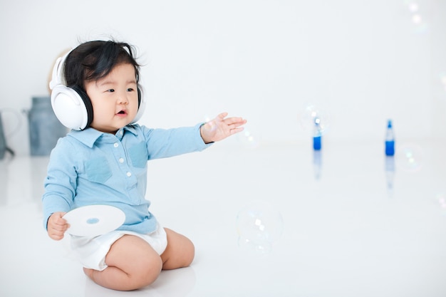 Un bébé avec des écouteurs sur une pièce blanche s'amuse.