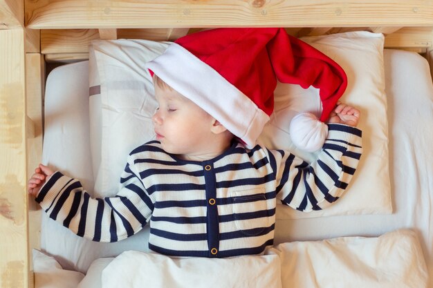 Bébé endormi en bonnet de Noel rouge dans son lit