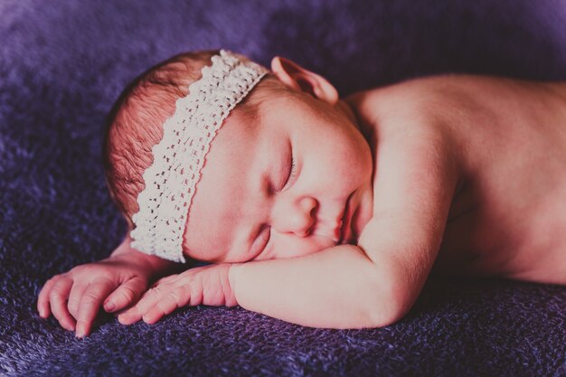 Bébé endormi avec une dentelle blanche sur la tête allongée sur le ventre sur une couverture violette