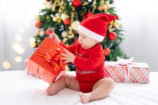 Bébé enfant heureux en costume de père Noël rouge célébrant le nouvel an à la maison avec arbre de Noël et cadeaux