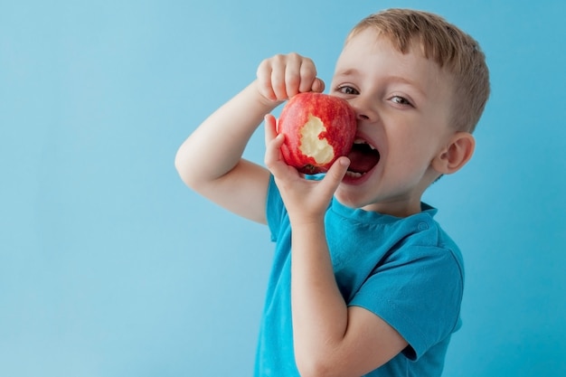 Bébé enfant tenant et mangeant une pomme rouge sur bleu