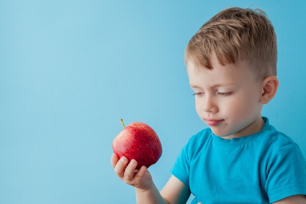 Bébé enfant tenant et mangeant une pomme rouge sur fond bleu, nourriture, alimentation et concept de saine alimentation