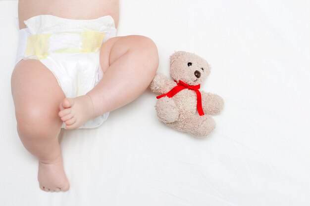 Le bébé est allongé sur un drap blanc et à côté d'un ours en peluche. Jambes d'un nouveau-né en gros plan.