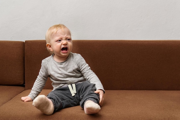 Bébé est assis sur le canapé et pleure Tout-petit malheureux et bruyant