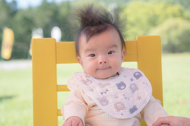 Un bébé est assis sur une chaise jaune avec un bavoir blanc qui dit "bébé" dessus