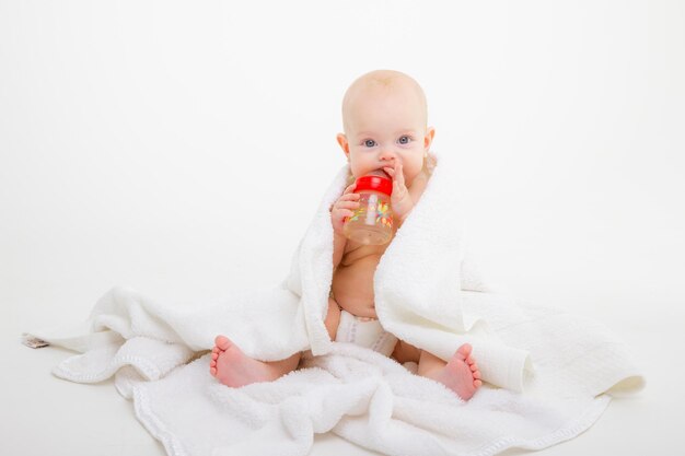Bébé est assis enveloppé dans une serviette tenant une bouteille d'eau potable sur un tournage en studio de fond blanc
