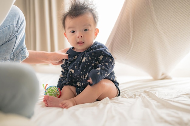 Un bébé est assis sur un lit avec une femme tenant un jouet.