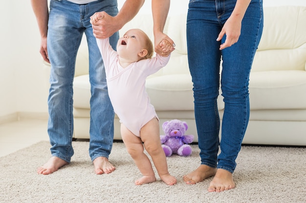 Bébé fait ses premiers pas avec l'aide de sa mère et de son père à la maison.