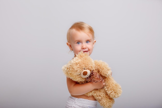 Bébé fille en couche jouant avec ours en peluche sur fond blanc