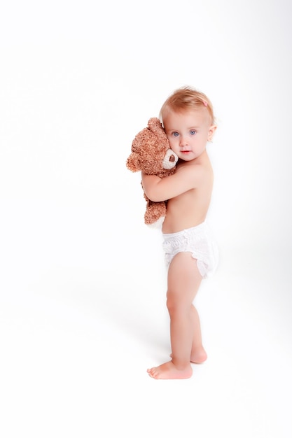 Bébé fille en couche tenant ours en peluche sur fond blanc