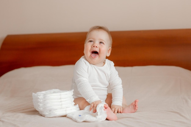 Bébé garçon assis sur le lit dans la chambre à côté de couches