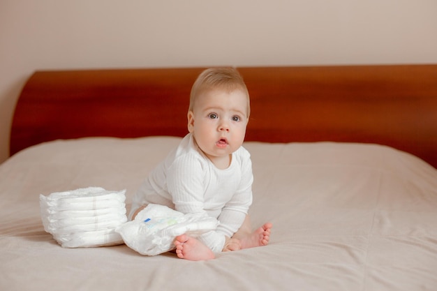 Bébé garçon assis sur le lit dans la chambre à côté de couches