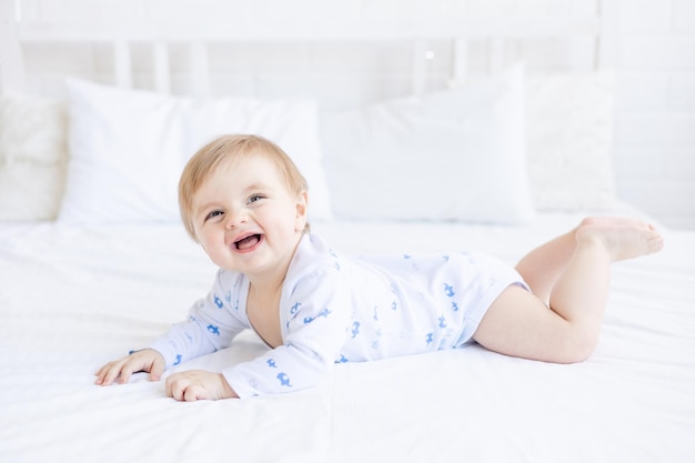 Un bébé garçon blond qui rit se trouve dans un berceau sur le ventre dans une chambre à la maison avec une literie en coton bleu et blanc et sourit le matin le concept de produits et accessoires pour enfants