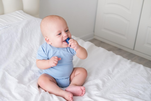 Bébé garçon chauve 3 mois en body bleu jouant avec des enfants cubes en bois jouets sur lit