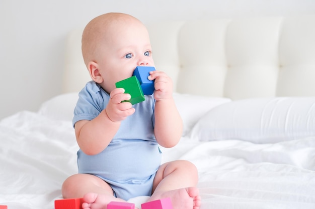 Bébé garçon chauve 3 mois en body bleu jouant avec des enfants cubes en bois jouets sur lit