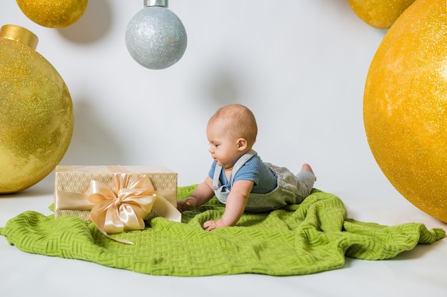 Bébé garçon couché sur le côté sur une couverture tricotée verte avec un cadeau sur blanc