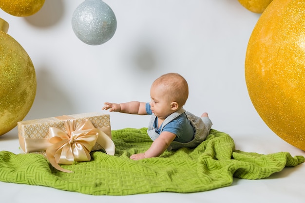 Bébé garçon couché sur le côté sur une couverture tricotée verte avec un cadeau sur blanc