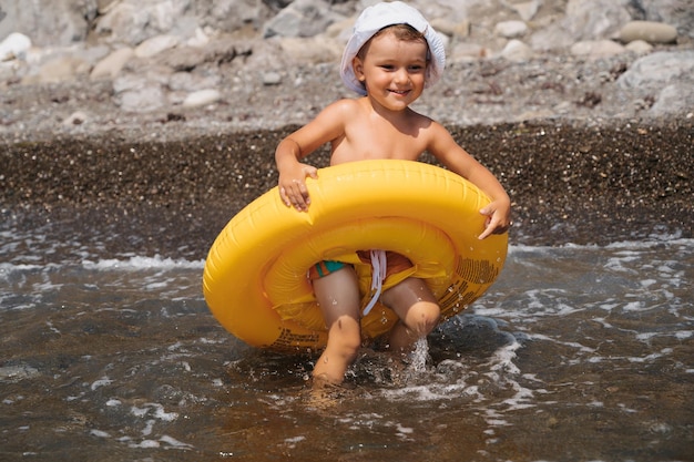 Bébé garçon court dans la mer dans un cercle gonflable jaune L'enfant se prépare à nager Il est heureux et rit
