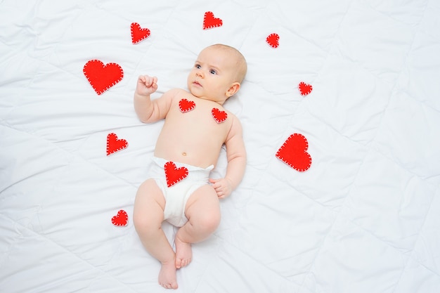 Bébé garçon dans une couche blanche se trouve contre les coeurs rouges aiment la Saint-Valentin