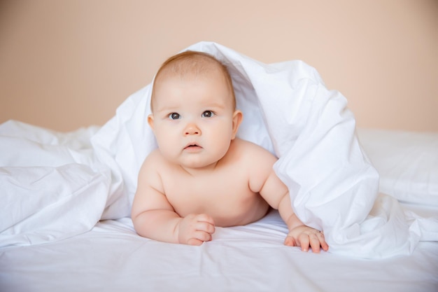 bébé garçon dans une couche est allongé sur un drap blanc, recouvert d'une couverture dans la chambre sur le lit