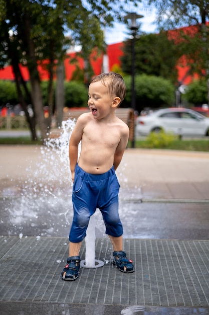 bébé garçon est debout dans la fontaine beaucoup d'éclaboussures l'enfant rit joyeusement