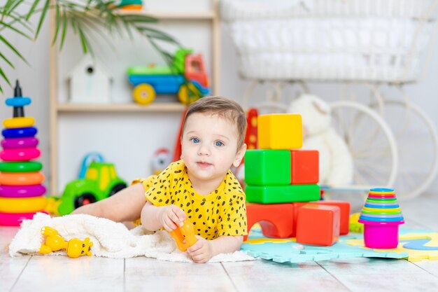 Bébé garçon joue dans la chambre des enfants dans un body jaune avec des jouets aux couleurs vives