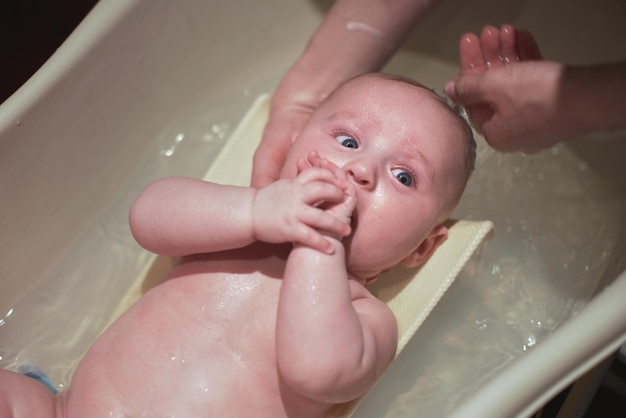 Bébé garçon lavé à l'intérieur dans une petite baignoire, mère tenant et se lavant la tête, vue d'en haut