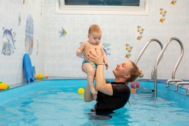 Bébé garçon s'entraîne à nager dans la piscine avec un entraîneur