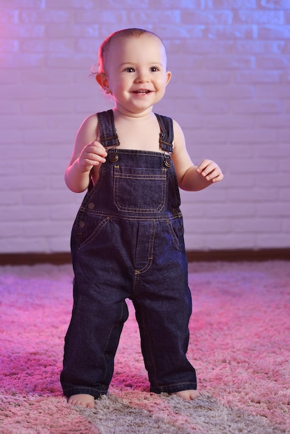 Photo bébé garçon en salopette en jean souriant tout en se tenant pieds nus