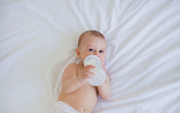 Bébé garçon se trouve sur une couverture en coton sur le lit et mange un mélange d'une bouteille