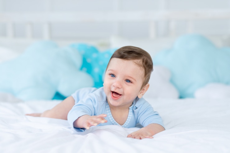 Photo bébé garçon souriant ou riant sur le lit pour dormir, petit bébé heureux en bonne santé en body bleu