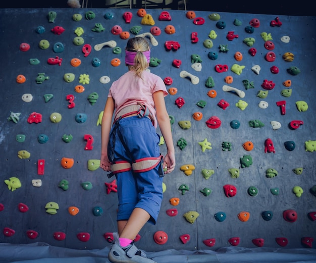 Photo un bébé grimpeur fort grimpe sur un mur artificiel avec des poignées et des cordes colorées