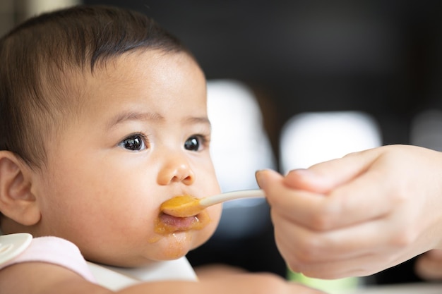 Un bébé heureux est assis dans une chaise d'enfant en train de manger son premier repas. Maman nourrit bébé.