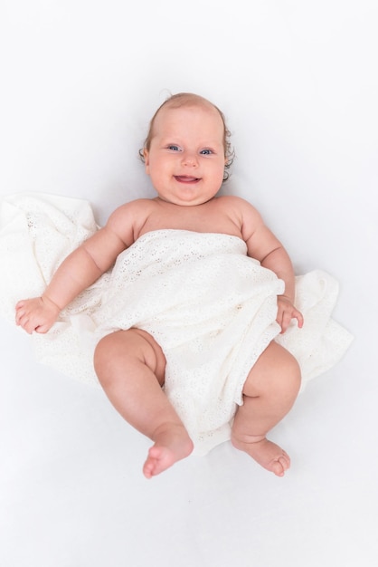 Le bébé heureux mignon se trouve sur une feuille blanche et est couvert d'un tissu de laine