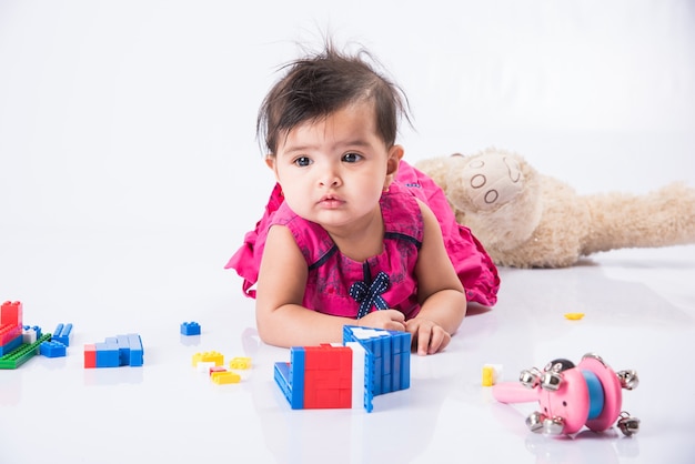 Bébé indien jouant avec des jouets ou des blocs, bébé asiatique jouant avec des jouets sur fond blanc, petite fille indienne jouant avec des jouets, bambin indien jouant avec des jouets en position couchée sur le sol