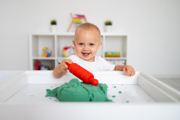 Photo bébé jouant avec du sable cinétique vert et rouleau à pâtisserie