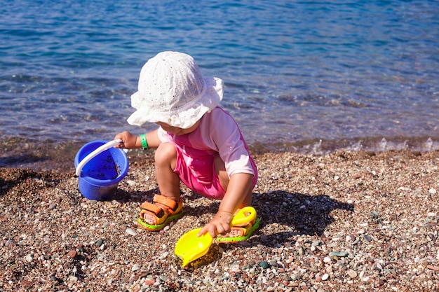 Bébé joue au bord de la mer avec des cailloux et un seau