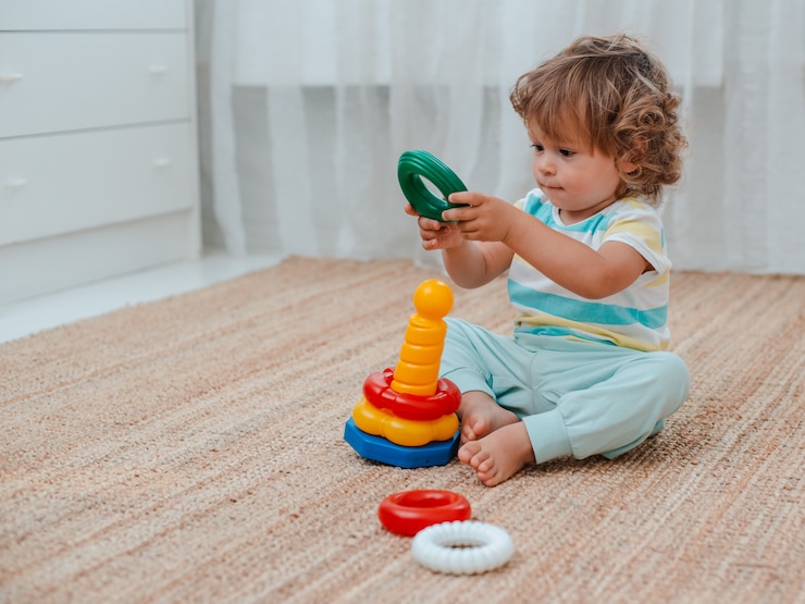 Photo bébé joue par terre dans la pièce avec des jouets en plastique éducatifs.