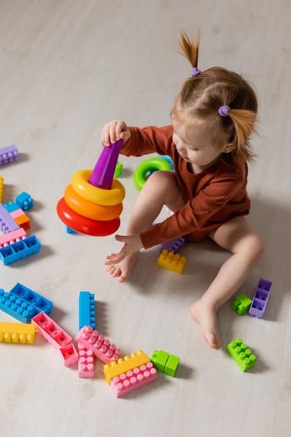 un bébé joyeux joue avec une pyramide multicolore et d'autres jouets éducatifs assis sur le sol