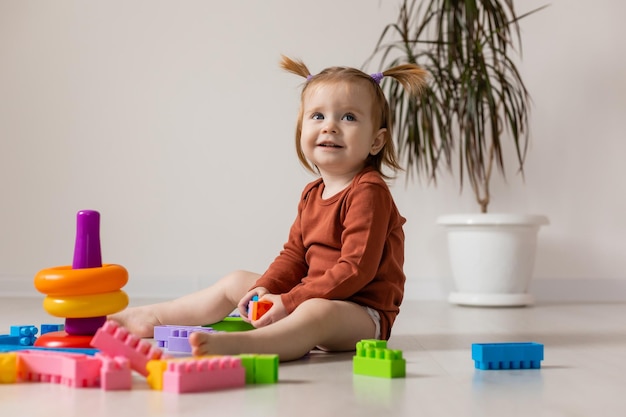 un bébé joyeux joue avec une pyramide multicolore et d'autres jouets éducatifs assis sur le sol