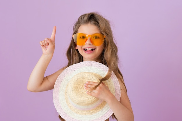 Un bébé à lunettes montre votre annonce et serre un chapeau de paille.