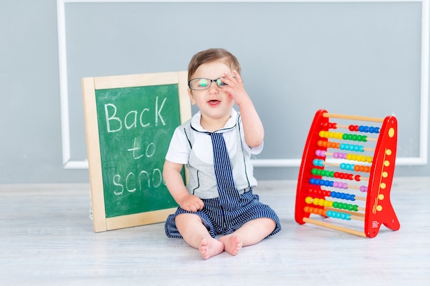 Un bébé avec des lunettes et un tableau noir qui dit bientôt à l'école est assis avec des factures