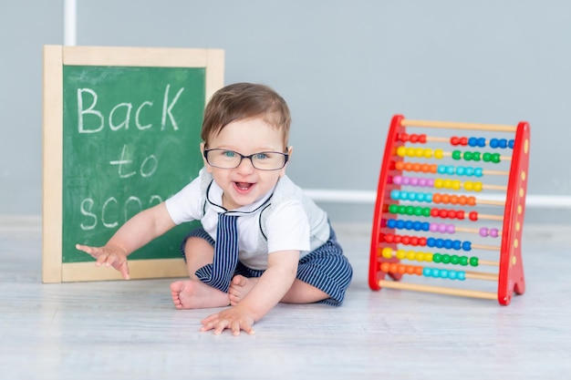 Un bébé avec des lunettes et un tableau noir qui dit bientôt à l'école est assis avec des factures