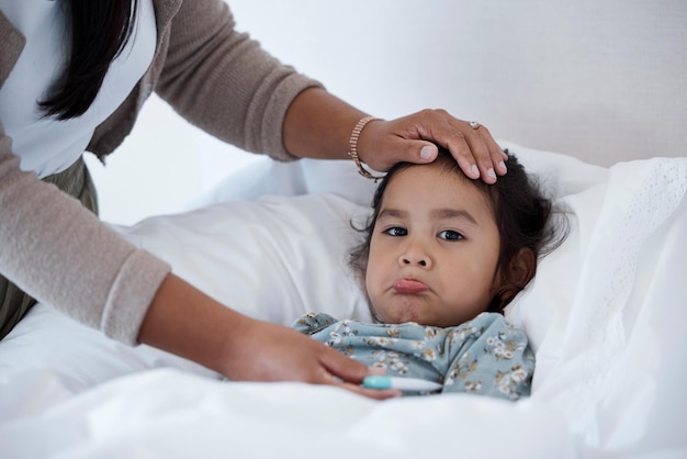 Bébé malade au lit avec les mains de la mère pour le soutien et l'amour de la garde d'enfants Fille triste à la maison en hiver avec un rhume ou une grippe et un parent maman ou femme aide et vérifie la température avec la main sur le front