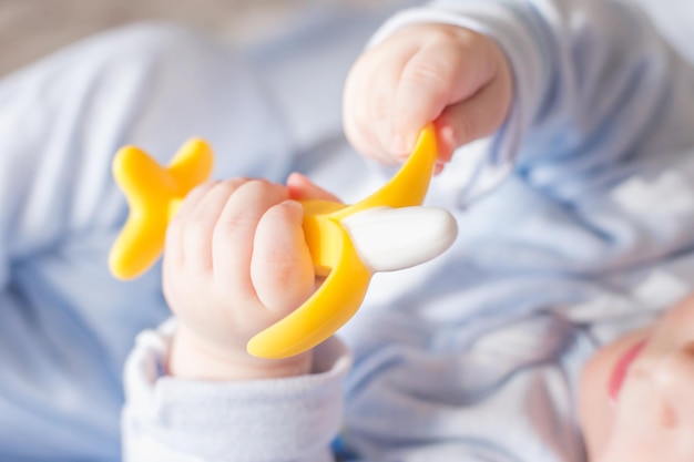 Bébé mâle tient un anneau de dentition banane dans sa main développement et massage des gencives gros plan anneau de dentition