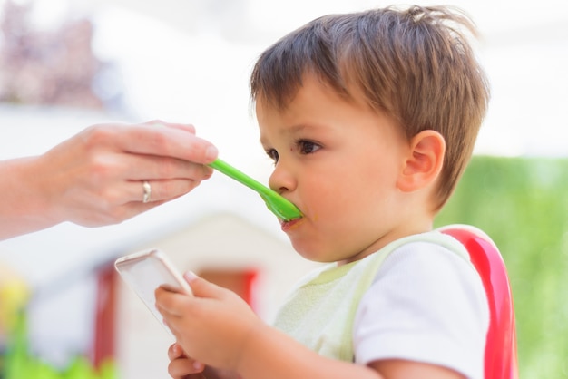 Bébé mange le déjeuner en regardant le smartphone