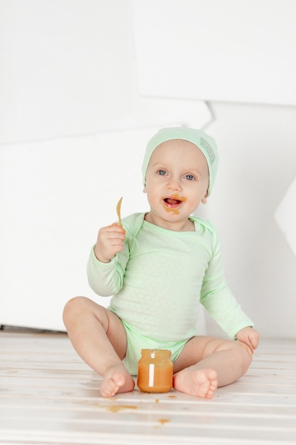 Bébé mange de la purée de fruits avec une cuillère dans un body vert, alimentation et concept d'aliments pour bébé