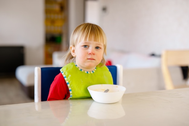 Bébé mignon 1,4 ans assis sur une chaise haute pour enfants et manger des légumes seuls dans la cuisine blanche.